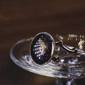 Silver ring with a dark purple cremation ash gemstone on a reflective surface